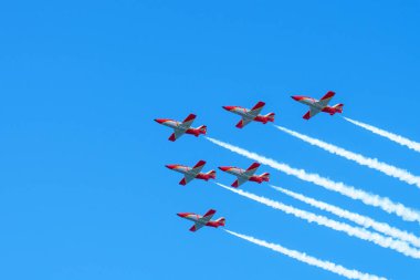 Gijon, İspanya - 24 Mayıs 2024: Altı kırmızı savaş uçağı açık mavi gökyüzünde beyaz duman izleri bırakarak formasyon içinde uçuyor