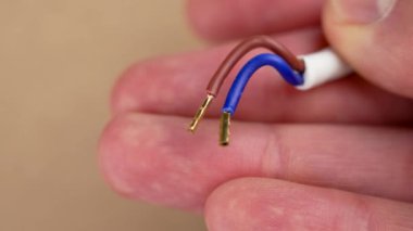 Kahverengi arka plandaki bir mühendisin elinde bakır uçlarla elektrik kablolarını bağlamaya hazır ve soyulmuş.