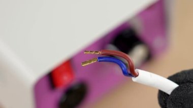 Elektrik kablolarının bakır terminalleri bir ölçüm cihazının arka planında koruyucu eldivenli bir elektrikçinin elinde.