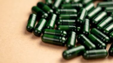Açık kahverengi bir yüzeye saçılmış yeşil bitkisel sağlık kapsülleri. Naturopati hapları. Döndürme