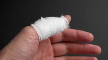 Yaralı baş parmağına sarılı beyaz bir bandajla kara bir arka plana sarılmış bir el. Yaralanma ve acı konsepti