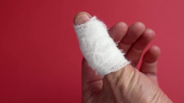 Yaralı başparmak beyaz bir bandajla sarılmış kırmızı arka planda acı ve yarayı sembolize ediyor. Kapat.