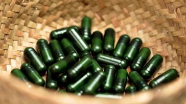 Organik çevre dostu hasır kasede bulunan yeşil tıbbi gıda kapsülleri yakın plan. Alternatif sağlık hizmeti kavramı. Döndürme