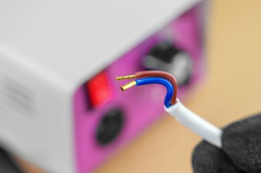 Siyah koruyucu eldivenli bir elektrikçinin elindeki kablolar, pembe kontrol paneli olan elektrikli bir manikür makinesinin arka planına bağlıydı.