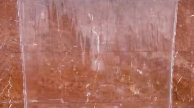 Temiz, serin bir su akıntısı kırmızı mermerden bir duvardan aşağı akar ve büyüleyici bir şelale şelalesi yaratır.