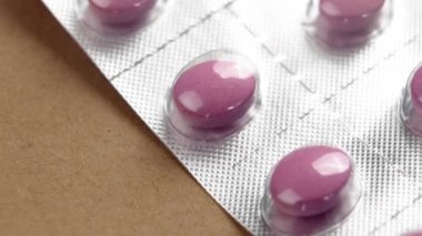 Pembe vitamin kompleksi hapları, kahverengi bir sehpanın üzerindeki ilacın pürüzsüz, parlak yüzeyiyle dolu bir pakette. Makro atış. Döndürme