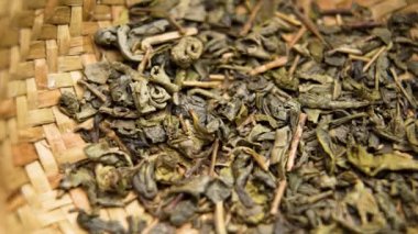 Kurumuş ve demlenmeye hazır yeşil çay yaprakları dokuma sepetinde oturup rahatlatıcı bir içeceğe dönüşmelerini beklerler. Makro atış. Döndürme