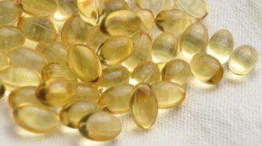 Yumuşak kumaş zemin üzerine diyet takviyeli softgel kapsülleri. Altın sarısı haplar. Beslenme hapları. Makro atış. Döndürme