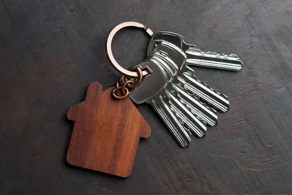 Karanlık bir yüzeydeki parlak tuşlara takılı anahtarlığı olan ahşap bir ev tılsımı.