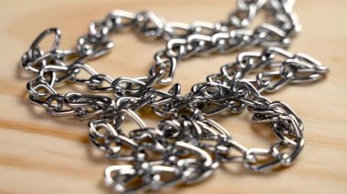 Parıldayan metal zincirlere detaylı bir bakış, mükemmel bir şekilde dolanmış, eşsiz dokularını ve ışıltılarını sıcak bir ahşap zemine vurguluyor. Döndürme
