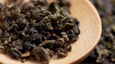 Tayvan 'ın yemyeşil dağlarından elde toplanmış Çin Oolong çayı. Tahta kaşıkta yeşil kurumuş yapraklar. Makro atış. Döndürme