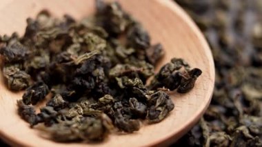Kurutulmuş yeşil oolong çay yaprakları yavaş çekimde tahta bir kaşığa yığılıyor.