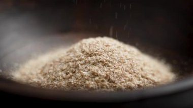Tıbbi isabgol ya da psyllium kabukları yavaş çekimde kahverengi ahşap bir kaseye dökülüyor.