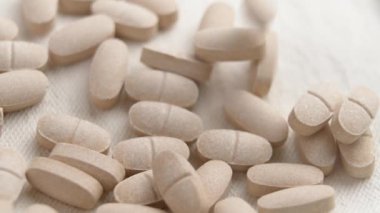 Birçok bej rengi yatıştırıcı bitkisel hap yavaş çekimde yumuşak bir kumaş arkaplana düşüyor.