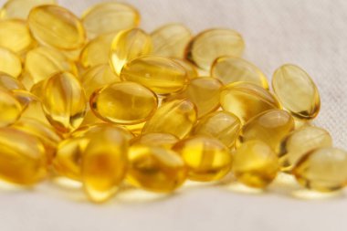Bej kumaş üzerinde D-3 vitamini içeren altın yumuşak jel kapsülleri. Beslenme takviyeleri. Makro çekim