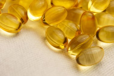 Yumuşak kumaş zemin üzerine diyet takviyeli softgel kapsülleri. Altın sarısı haplar. Beslenme hapları. Makro çekim