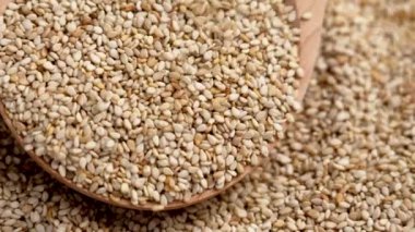 Çiğ organik susam tohumları tahta kaşıkta yığının üzerine düşüyor. Ağır çekim. Döndürme