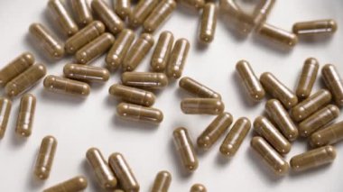 Tıbbi şifalı bitkisel kapsüller ya da takviyeler yavaş çekimde seramik mat hafif yüzeyine düşüyor. Döndürme