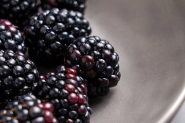 Gri seramik tabakta siyah böğürtlen. Taze, sulu organik böğürtlen. Sağlıklı malzeme. Makro