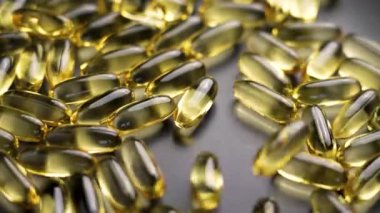 Sarı Omega-3 balık yağı kapsülleri gri bir tabağa düşüyor. Doymamış yağ asitleriyle yarı saydam takviyeler. Ağır çekim. Makro atış. Sağlıklı yaşam tarzı kavramı