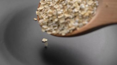 Çiğ yulaf ezmesi, tahılları siyah bir mutfak tabağında, tahta bir kaşıktan dağıttı. Organik kahvaltı lapası.