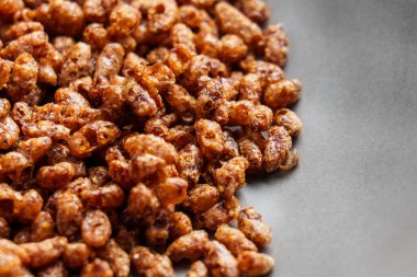 Çikolatalı, çıtır çıtır pirinç kahvaltı gevrekleri siyah bir tabağa saçılmış.