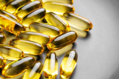 Gri seramik tabakta enerji ve refah için altın saydam doğal softgel kapsüllerinde Omega 3 takviyesi. Makro çekim