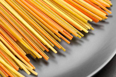 Doğal malzemelerden türetilmiş çarpıcı renkler içeren pişirilmemiş makarna, modern gri bir tabakta zarif bir şekilde düzenlenmiş.