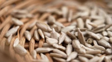 Çiğ ayçiçeği çekirdekleri kabuklarından soyulmuş ve ağır çekimde örülmüş ahşap bir sepetin içine düşmüş. Döndürme. Makro çekim