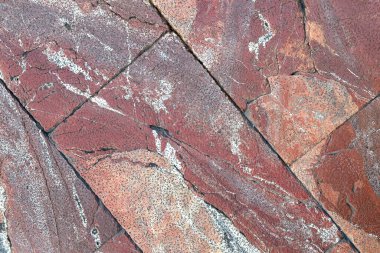 Kırmızı ve kahverengi zemin taş yüzeyinin soyut ve karmaşık dokuları ve renkleri benzersiz desenleri vurguluyor. Sert arkaplan