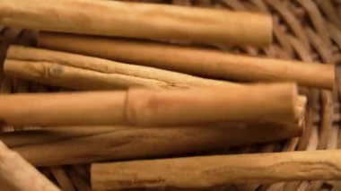 Organik kokulu tarçın çubukları yavaş çekimde sade örülmüş bir sepetin içine düşüyor.