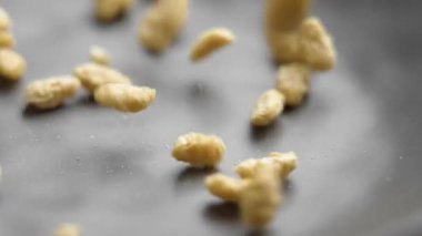İşlenmiş kuru yulaf taneleri ağır çekimde gri mutfak kasesine düşüyor. Kahvaltılık gevreğin organik besin bileşeni.