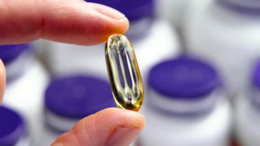 İlaç şişelerinin arka planına karşı eczacı ya da eczacı elinde Omega 3 takviye kapsülü. Makro çekim