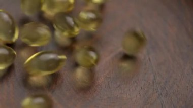 Morina yağının altın besin değeri yarı saydam kapsülleri yavaş çekimde ahşap bir çevre dostu konteynıra düşüyor. Makro atış. Vitamin dengesi için organik besin takviyeleri