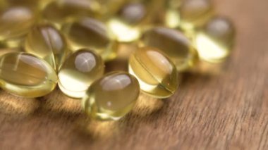 Altın morina yağı kapsülleri ahşap bir masaya saçılmış. Omega-3 kaynağı ve takviyelerde A vitamini. Doğal sağlık tedavileri. Makro. Döndürme