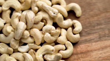 Ahşap bir masaya serpilmiş kaju fıstıkları kremalı ve pürüzsüz bir dokuya sahiptir. Sağlıklı bir aperatif ya da tarif malzemesi için idealdir. Döndürme