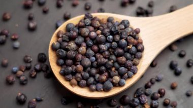 Kurutulmuş ardıç meyveleriyle dolu ahşap kaşık geleneksel ve doğal yemeklerde antioksidan zengini bir süper yiyecek baharatı sergiliyor. Döndürme. Üst görünüm