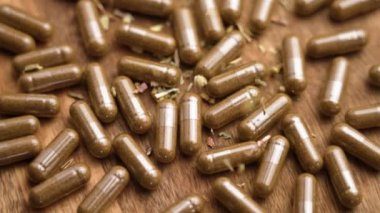 Bitkisel destek kapsüllerinin üzerine kurumuş kiriş otları dökülüyor. Bitkisel ilaçlar ve doğal sağlık konsepti. Ağır çekim. Döndürme