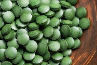 Tahta bir kasede yeşil spirulina hapları yakın plan. Besin yoğunluğundaki yosunlardan sağlıklı detoks faydaları olan doğal besleyici haplar.