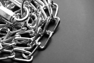 Metal zincirler, siyah bir zemin üzerine karmaşık desenlerle ışık ve dokularla sarmalanır. Makro