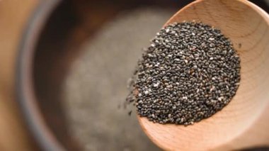 Chia tohumları ahşap bir kaşıktan dökülüp zengin dokuları ve organik kaliteyi yakalıyor. Meyve püresi, puding ve sağlıklı tarifler için mükemmel. Sağlıklı beslenme kavramı. Yavaş çekim
