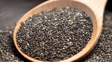 Ahşap kaşıkta chia tohumları, temiz yemek, fitness diyeti ve antioksidan zengini tarifler için etrafa saçılmış. Döndürme