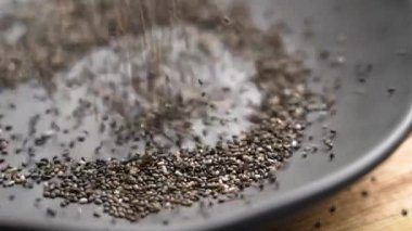 Chia tohumları koyu gri bir kaseye dökülüyor. Besleyici zenginlik ve keto yemeklerinde sağlıklı beslenme ve sağlık destekleri için ideal kullanım. Yavaş çekim