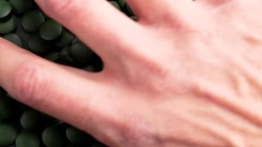 Bir avuç dolusu yeşil spirulina tableti döker. Protein, vitamin ve antioksidan açısından zengin alglerden elde edilen doğal destek hapları. Sağlık ve refahı arttırır.
