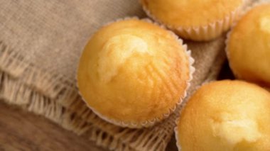 Kağıt ambalajlı altın kekler. Kırsal alanda yeni pişmiş ve kabarık, çiğ çuval bezi ve yaşlandırılmış tahta. Kahvaltı ya da tatlı için mükemmel bir ziyafet. Döndürme. Üst görünüm