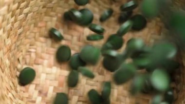 Dokuma sepetine dökülen yeşil spirulina tabletleri. Enerji ve bağışıklık desteğini arttırmak için organik takviyelerin besin yoğunluğu ve sağlık faydaları. Ağır çekim. Üst görünüm