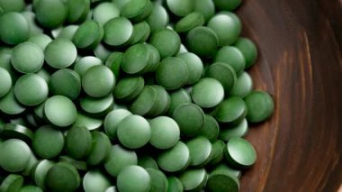 Tahta bir kasede canlı yeşil spirulina hapları. Temel besinlerle dolu bu tabletler bağışıklığı, enerjiyi ve genel sağlığı destekliyor. Döndürme. Üst görünüm