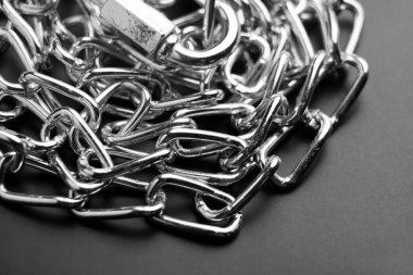 Kelepçeli metal zincir düzgün bir yığına dizilmiş. Pürüzsüz cilalanmış bağlantılar ve güvenli klipler siyah üzerine işlevsel ama dekoratif bir öge oluşturur