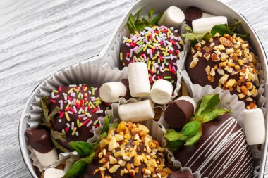 A festive assortment of chocolate-covered strawberries topped with sprinkles, nuts and marshmallows, presented in heart-shaped box. Perfect for gifting clipart