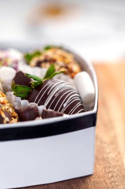 Vertical close-up of heart-shaped box showcasing handcrafted chocolate-coated strawberries. A single berry is adorned with white sweet drizzle and fresh green leaves. Premium organic treats  clipart